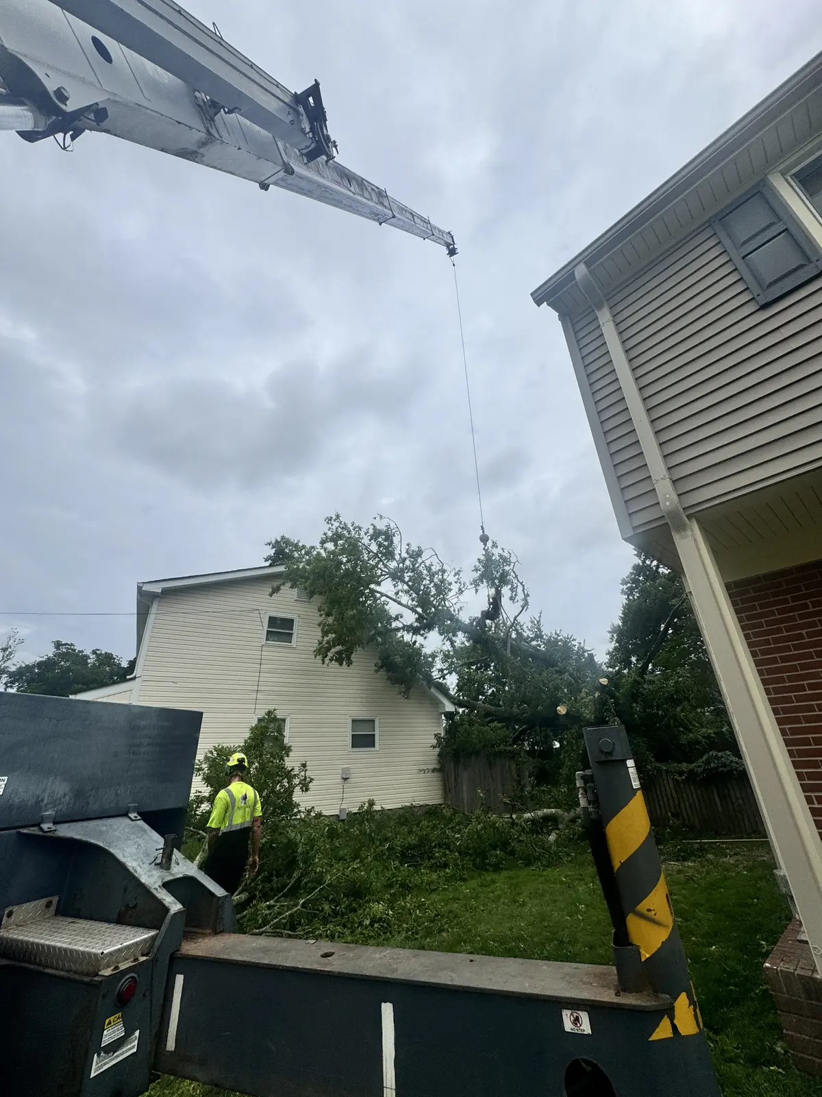 Crane truck set up with outriggers down and boom extended over a house for a tree removal in Kempsville, Virginia Beach, VA